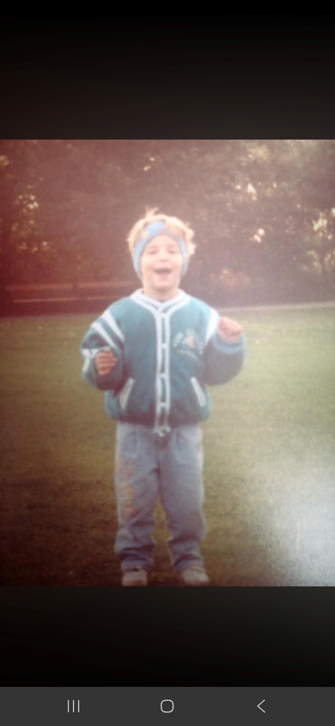 Kindheitsfoto im Garten mit weiter Jacke und buntem Stirnband.